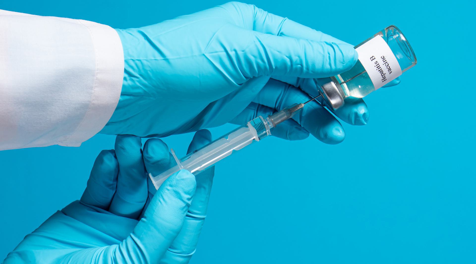 Hepatitis B Vaccine Gloved hands holding a syringe and a vial labeled 'Hepatitis B vaccine' against a blue background.
