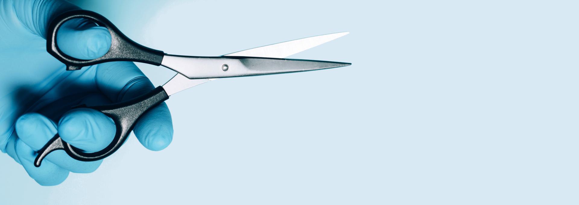 Propofol Hair Follicle Drug Test Hand in blue glove holding a pair of scissors against a light blue background.