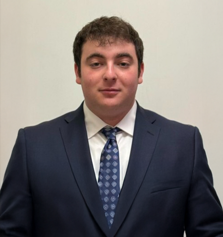Josh (Software Engineer) Josh in a suit with a patterned tie against a plain background.