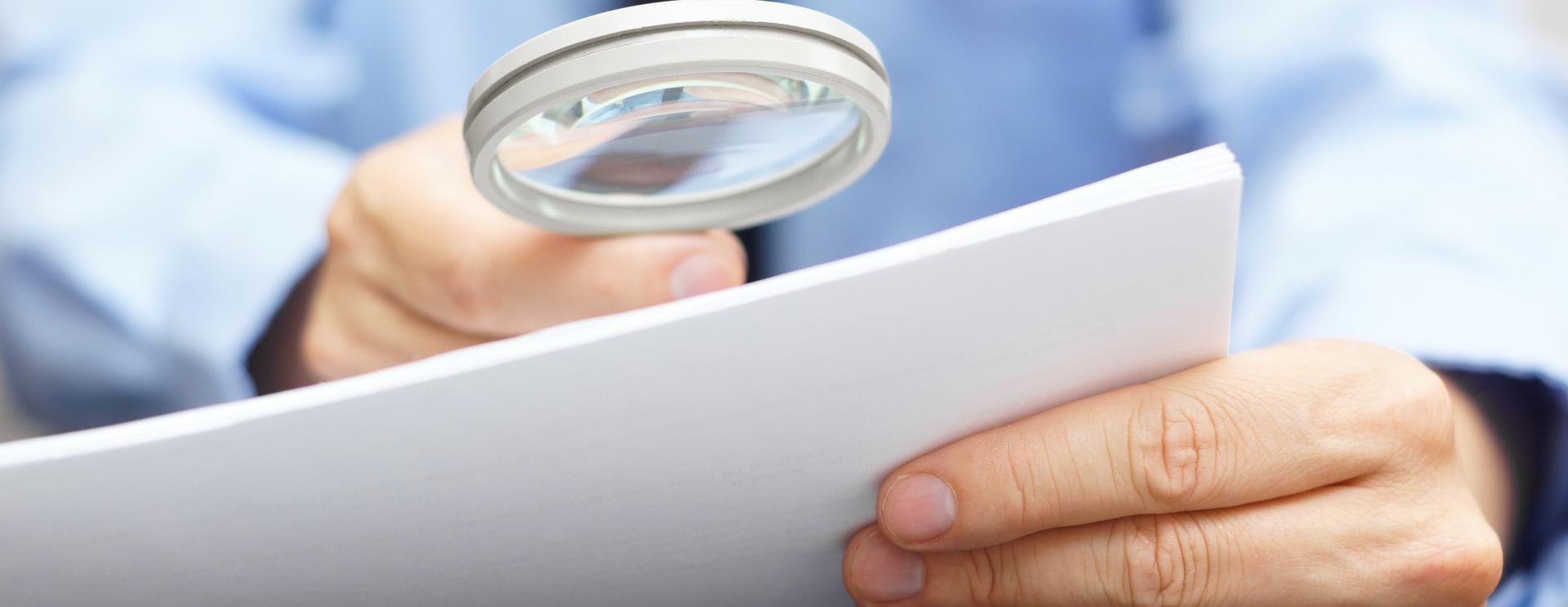 Person examining a document with a magnifying glass.