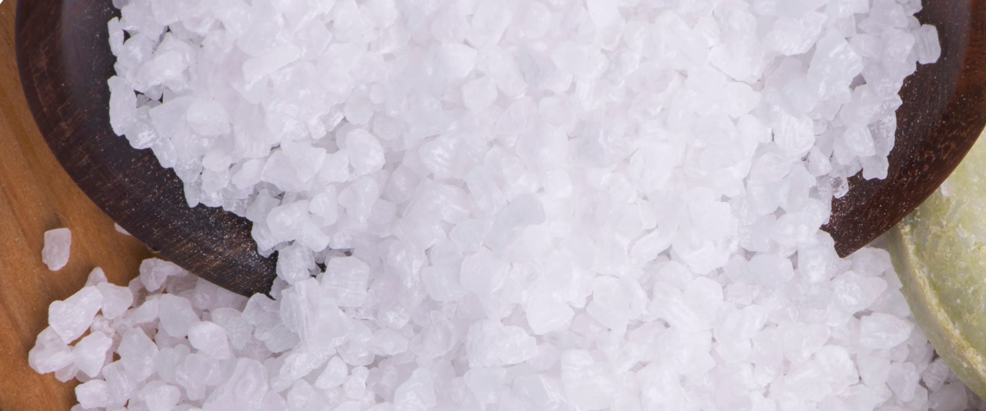 Close-up of coarse bath salt crystals in a wooden spoon on a wooden surface.