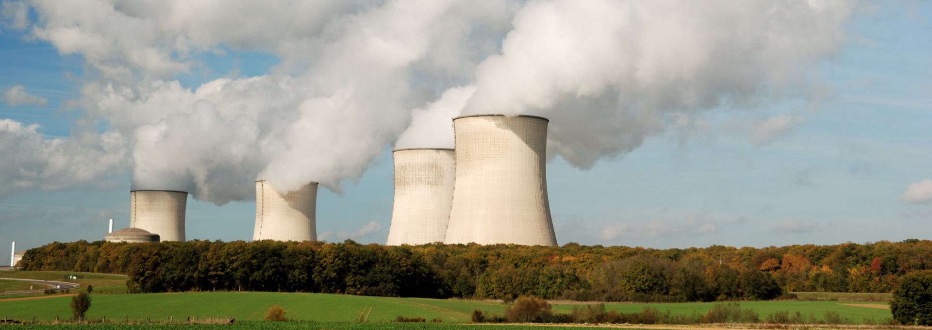NRC Drug Test (Nuclear Regulatory Commission) Nuclear power plant cooling towers emitting steam against a blue sky, surrounded by green fields and trees.