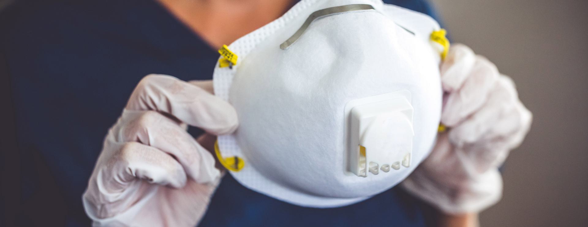 Respirator Fit Test (Qualitative) Person wearing gloves holding an N95 mask with a valve.
