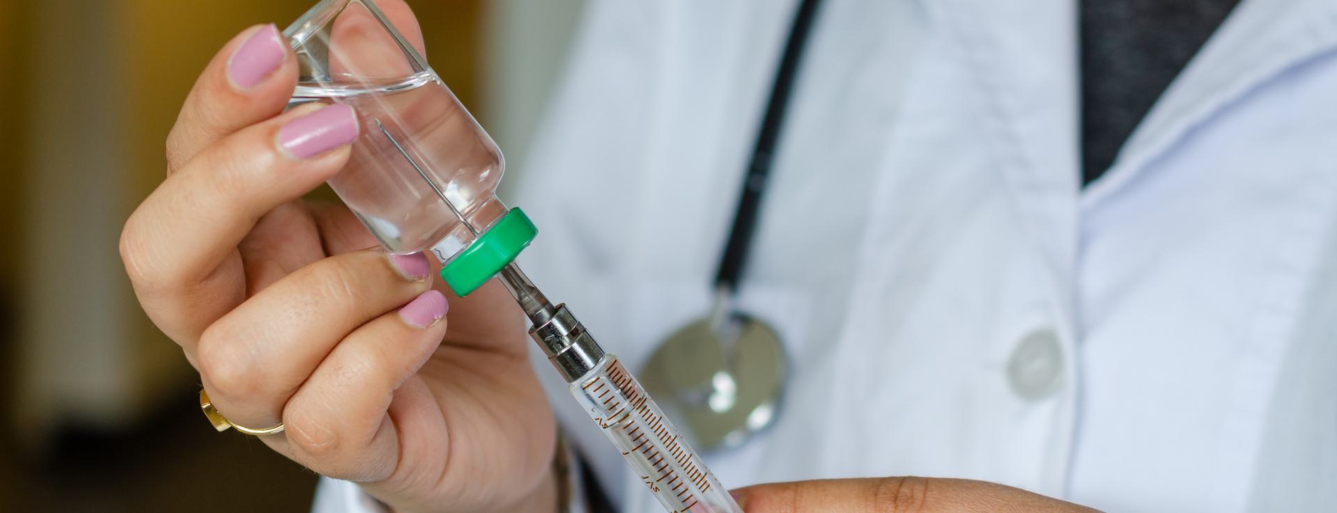 MMR Vaccine Healthcare professional drawing liquid from a vial into a syringe, wearing a white coat and stethoscope.