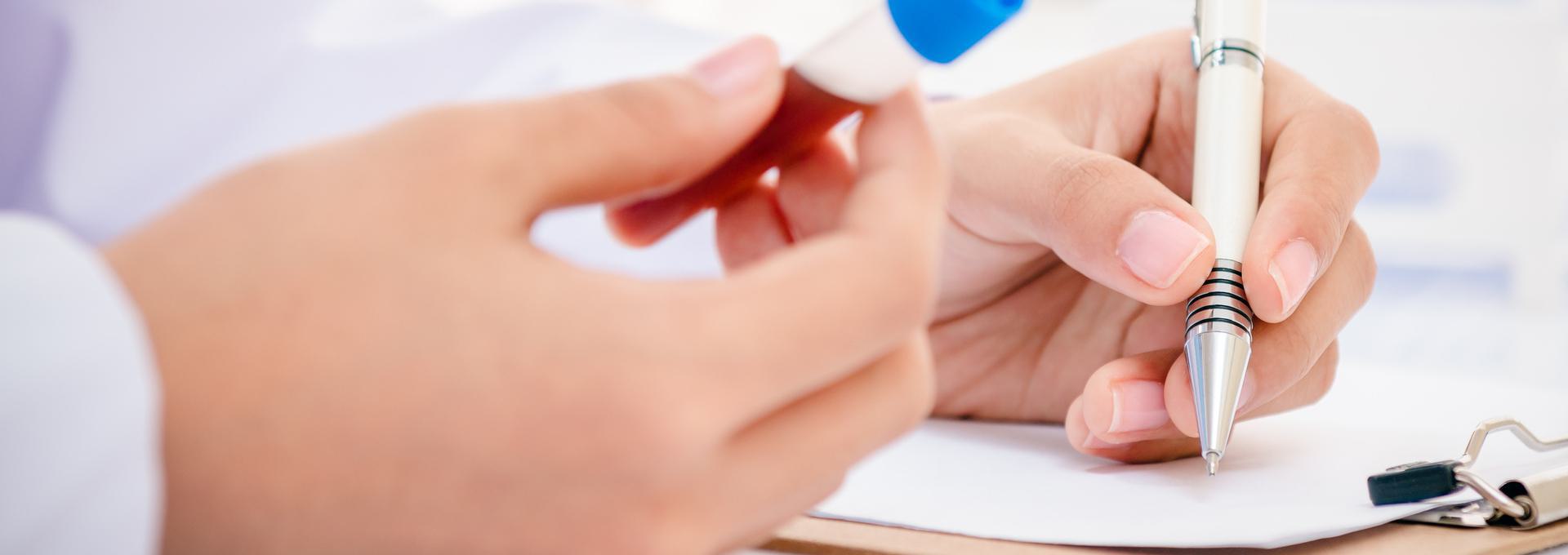 MMR Titer Close-up of hands holding a pen and a test tube with blue cap, writing on paper.
