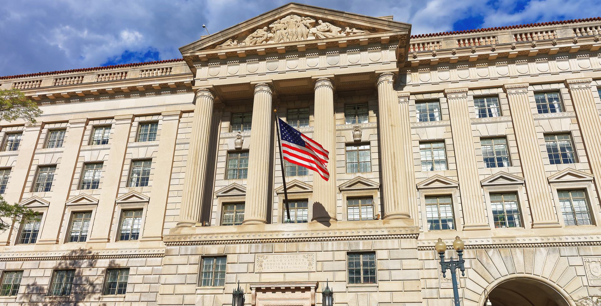 OIG Sanctions Historic government building with American flag, featuring classical architecture and columns under a blue sky.
