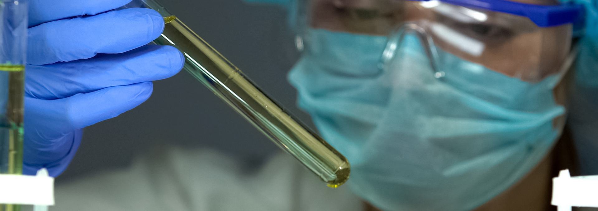 Scientist wearing protective gear examining a test tube with yellow liquid.