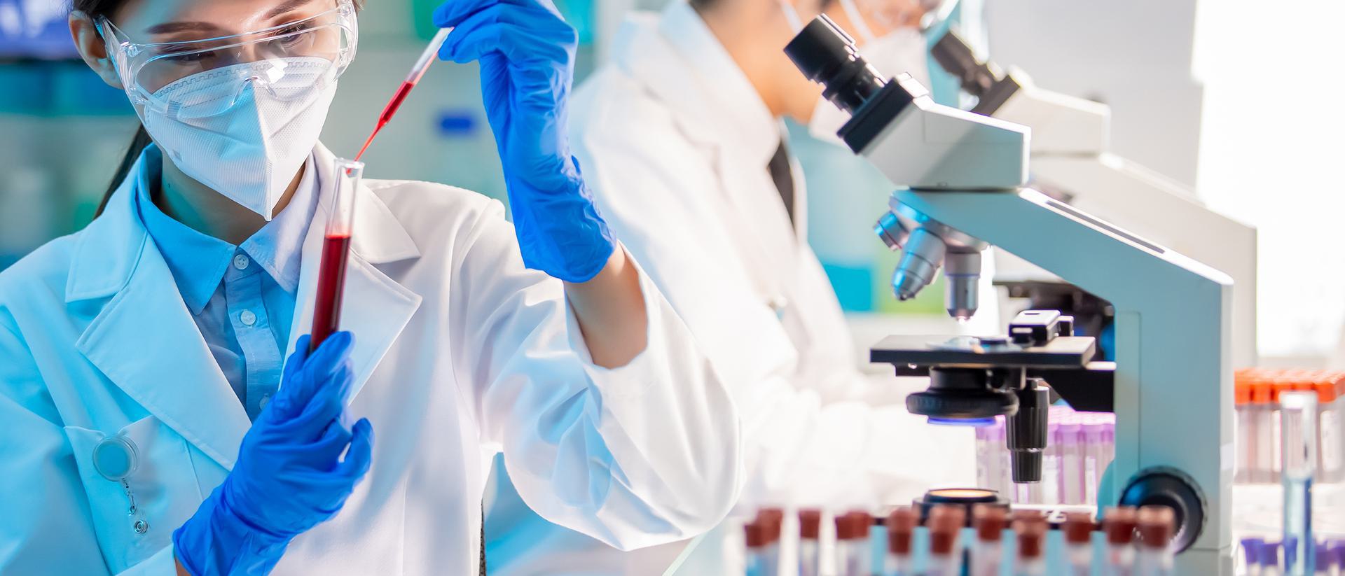 Hepatitis B Antibody Test Scientist in a lab coat and protective gear using a pipette to transfer red liquid into a test tube, with microscopes in the background.