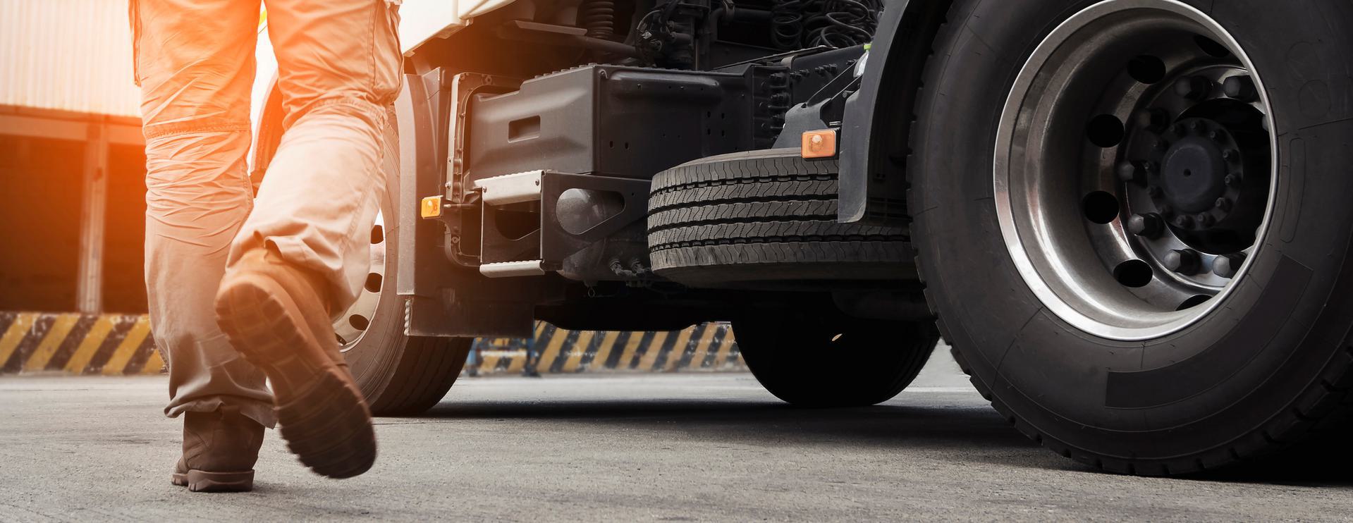 DOT Driver Pamphlet Person walking towards a large truck with visible wheels and chassis in an industrial setting.