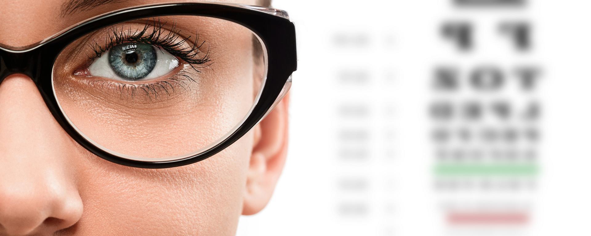 Close-up of a person's eye wearing glasses with an eye chart in the background.