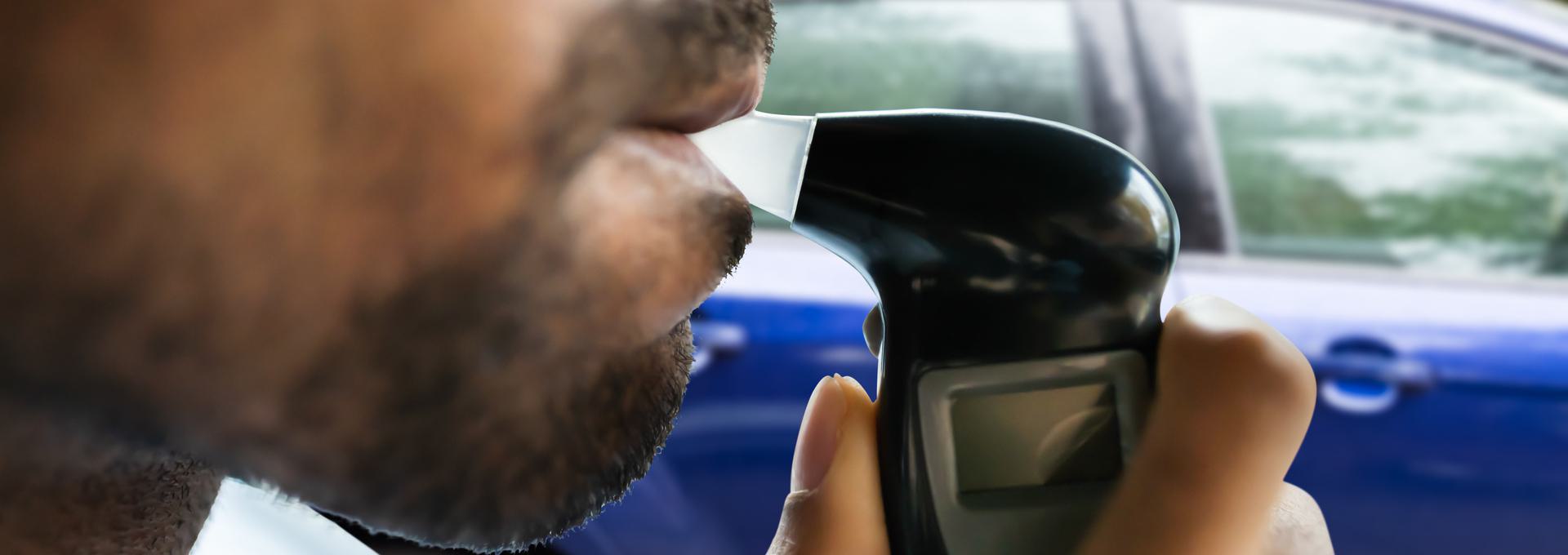 Non-DOT Breath Alcohol Testing Person using a breathalyzer device near a car.