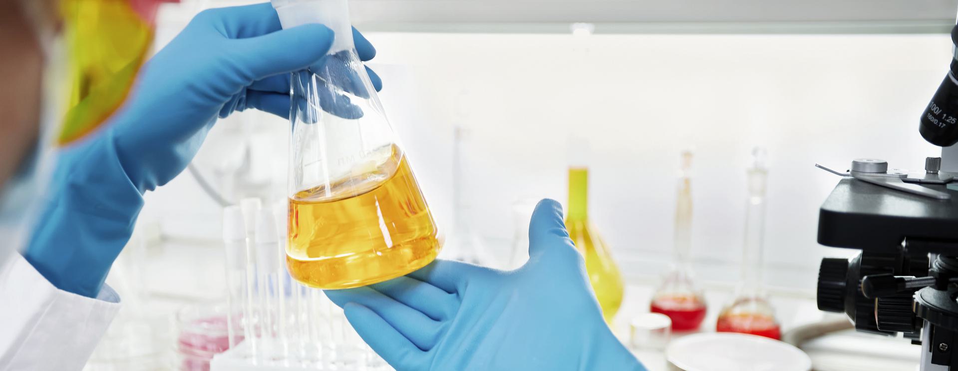 22 Panel Urine Drug Test Scientist wearing blue gloves examining a flask with yellow liquid in a laboratory setting.