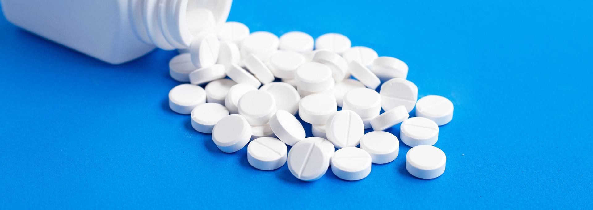 White pills scattered from a bottle on a blue surface.