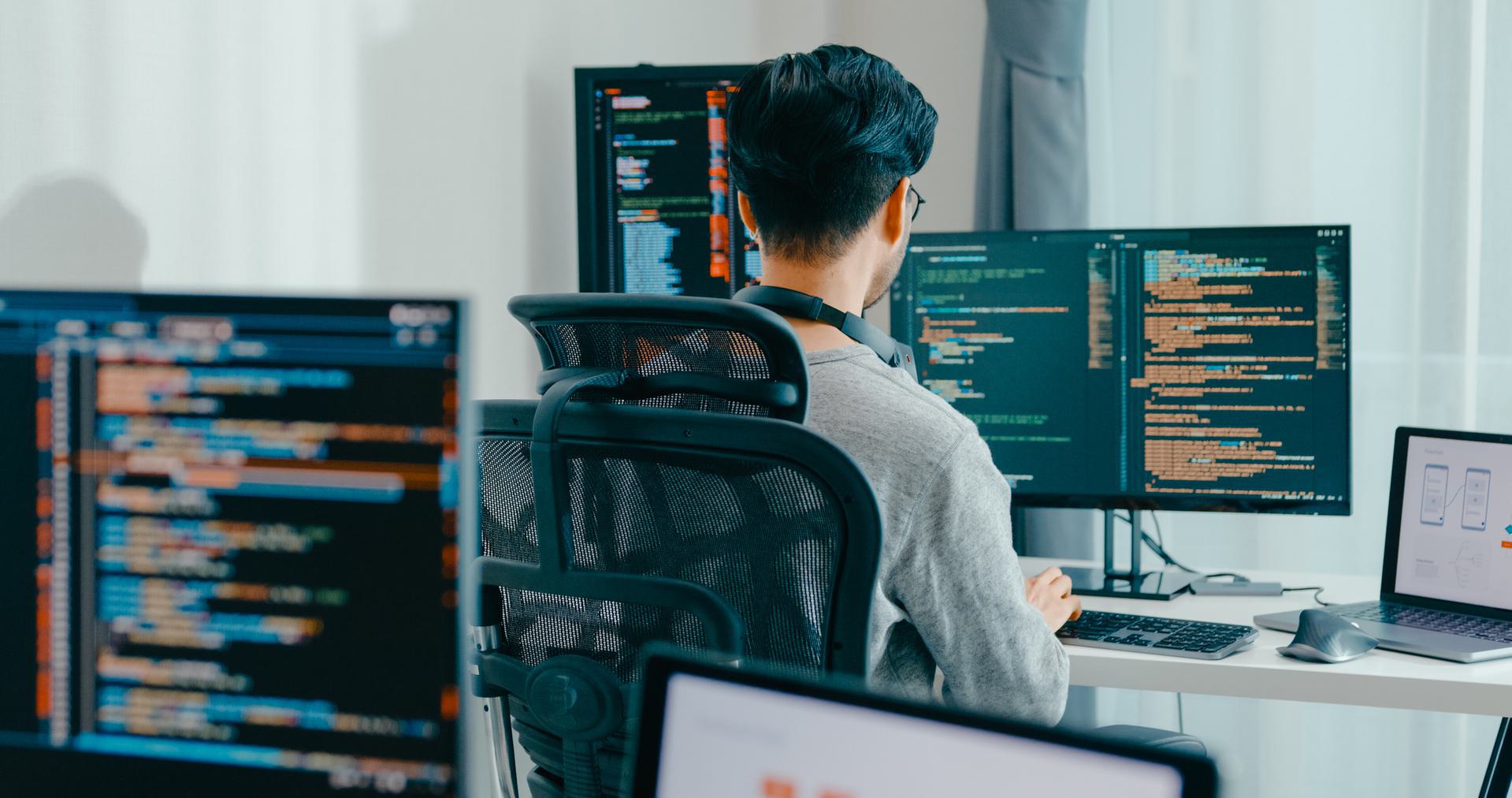 Software Developer at Work Person working at a desk with multiple computer monitors displaying code.