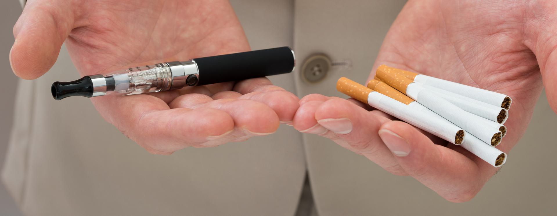 Nicotine Test Person holding an e-cigarette in one hand and traditional cigarettes in the other.