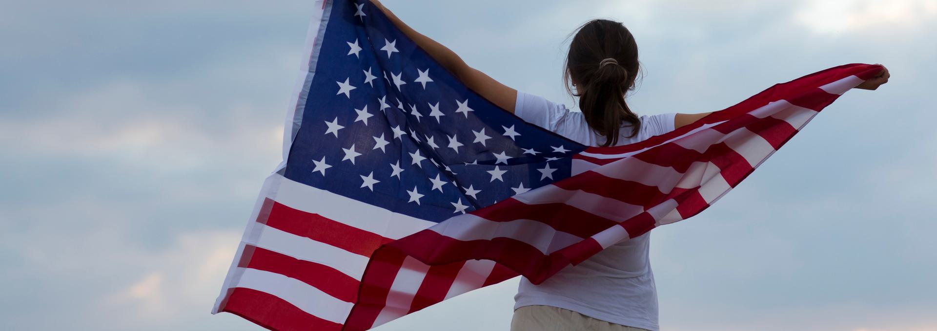 Immigration DNA Testing Person holding an American flag against a cloudy sky.