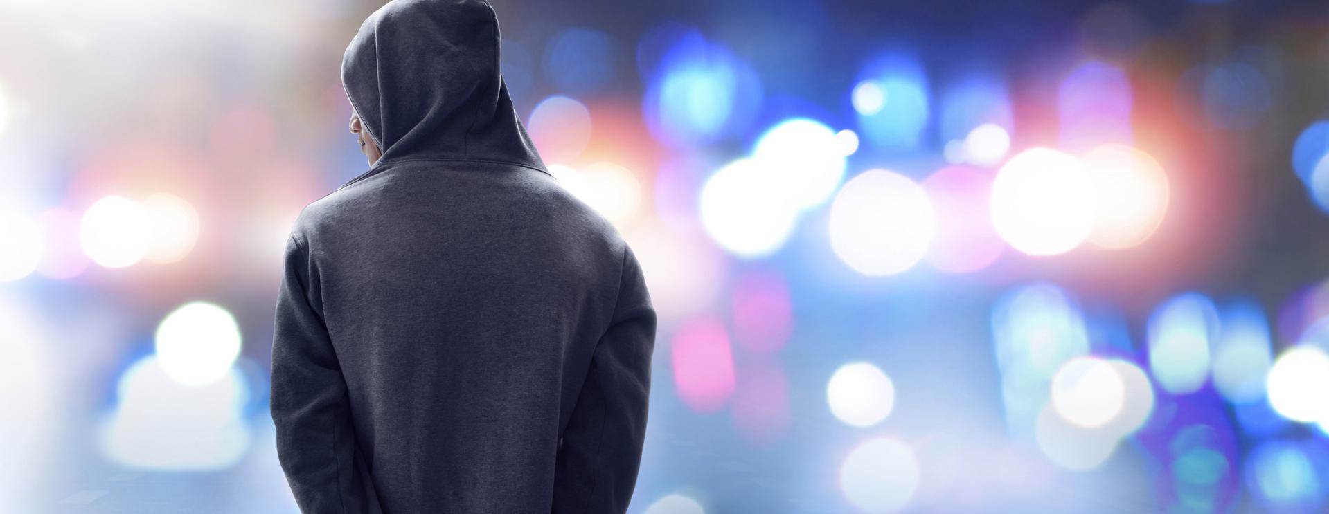 Person in a hoodie standing with their back to the camera, against a blurred background of colorful lights.