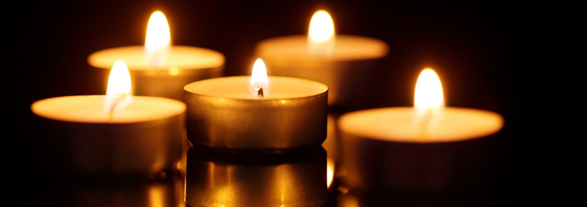 Five lit tealight candles glowing in the dark.