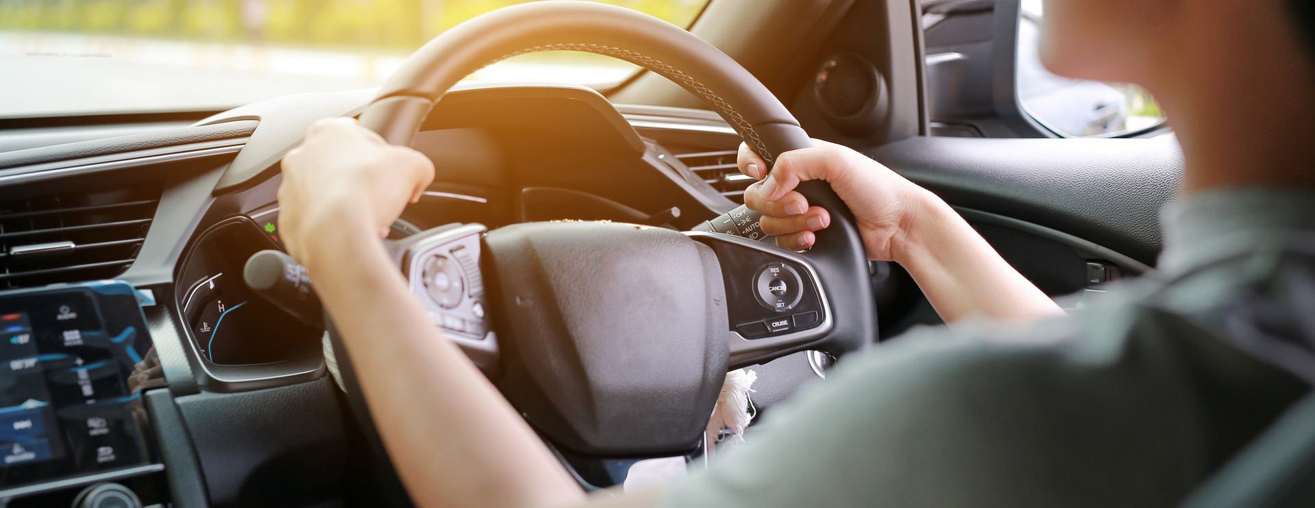 Motor Vehicle Records (MVR) Check Person driving a car, hands on steering wheel with dashboard visible.
